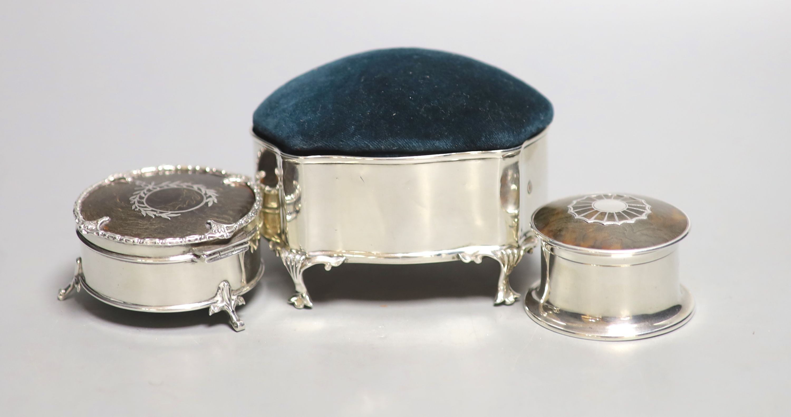 An Edwardian silver mounted pin cushion, Birmingham, 1909, length 10cm and two George V silver and tortoiseshell pique circular trinket boxes.